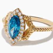 The 14K Yellow Gold Blue and White Diamond Marquise Ring features a striking blue and white diamond centerpiece, accented by a halo of round white diamonds and detailed band craftsmanship.
