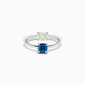The 14K White Gold Blue and White Diamond Split Shank Ring features a clear oval and blue cushion-cut gemstone set side by side on a minimalist band, showcasing striking contrast between the blue and white diamond accents.