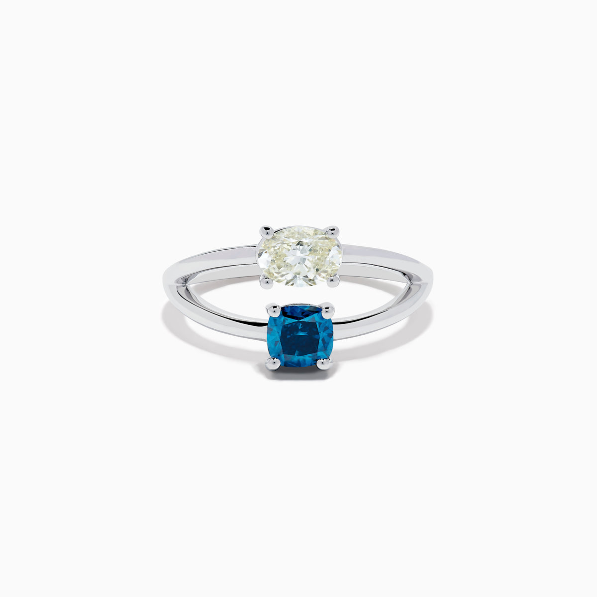 The 14K White Gold Blue and White Diamond Split Shank Ring features a clear oval and blue cushion-cut gemstone set side by side on a minimalist band, showcasing striking contrast between the blue and white diamond accents.