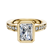 The 18K Yellow Gold Bezel Full Bezel North/South Classic Flat 1-Row-Pave 2.5mm Engagement Ring features a large radiant-cut center stone in a gold bezel, with small round diamonds set along both sides of the band.