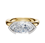 A 14K two-tone Bezel Half Bezel East/West Classic Dome 3.0mm engagement ring, featuring a marquise-cut diamond in a distinctive four-prong setting, is displayed against a plain white background.