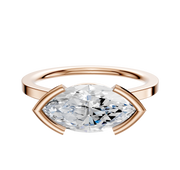 A 14K rose gold bezel half bezel east/west cathedral flat 1.5mm engagement ring is shown with a horizontally set marquise-cut diamond on a plain white background.