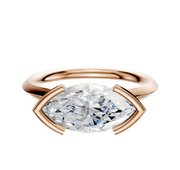 A 14K rose gold bezel half bezel east/west cathedral knife edge 2.0mm engagement ring is displayed against a white background, featuring a modern open setting with a marquise-cut diamond.