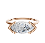 An 18K rose gold bezel half bezel east/west classic knife edge 1.5mm engagement ring with a large marquise-cut clear diamond, set against a plain white background.