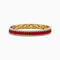The 18K Yellow Gold Ruby and Diamond Bangle features a honeycomb-patterned interior, with a row of rubies bordered by two rows of sparkling diamonds on the outside.