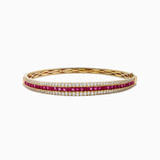 The Ruby Royale 14K Yellow Gold Ruby and Diamond Bangle features two rows of sparkling diamonds flanking a central row of square-cut rubies for a symmetrical, elegant design.