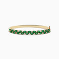 The 14K Yellow Gold Emerald and Diamond Bangle features two rows of round emeralds bordered by smaller diamonds, with a side clasp.