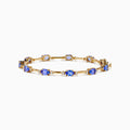 The 14K Yellow Gold Tanzanite and Diamond Station Bracelet showcases evenly spaced oval tanzanites set in gold links, each accented by sparkling diamonds, creating an elegant look against a white background.