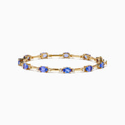 The 14K Yellow Gold Tanzanite and Diamond Station Bracelet showcases evenly spaced oval tanzanites set in gold links, each accented by sparkling diamonds, creating an elegant look against a white background.