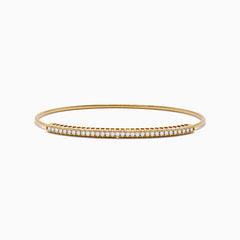 The 14K Yellow Gold Flexible Diamond Bangle features a slender design with sparkling diamonds set along the top half, shown against a white background.