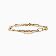 A 14K yellow gold paperclip chain bracelet featuring elongated textured links and a heart charm at the center, displayed on a white background.