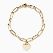 A 14K yellow gold paperclip chain bracelet featuring elongated textured links and a heart charm at the center, displayed on a white background.