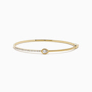 The D'Oro 14K Yellow Gold Pear Bezel Diamond Bangle showcases a row of small diamonds and a central pear bezel-set gem, all elegantly displayed against a plain white background.