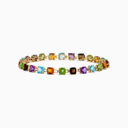 The 14K Yellow Gold Cushion Cut Multi Color Gemstone Tennis Bracelet showcases a row of cushion-cut multicolored gemstones set in yellow gold, displayed against a white background.