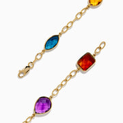 The Mosaic 14K Yellow Gold Multi Gemstone Station Bracelet features five colorful gemstones—blue, green, orange, red, and purple—in various shapes along a gold chain. Shown on a white background, it’s a vibrant accessory for any occasion.