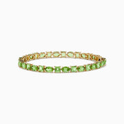 The 14K Yellow Gold Peridot Tennis Bracelet 13.50 TCW features evenly spaced round and square green gems, shown against a white background.