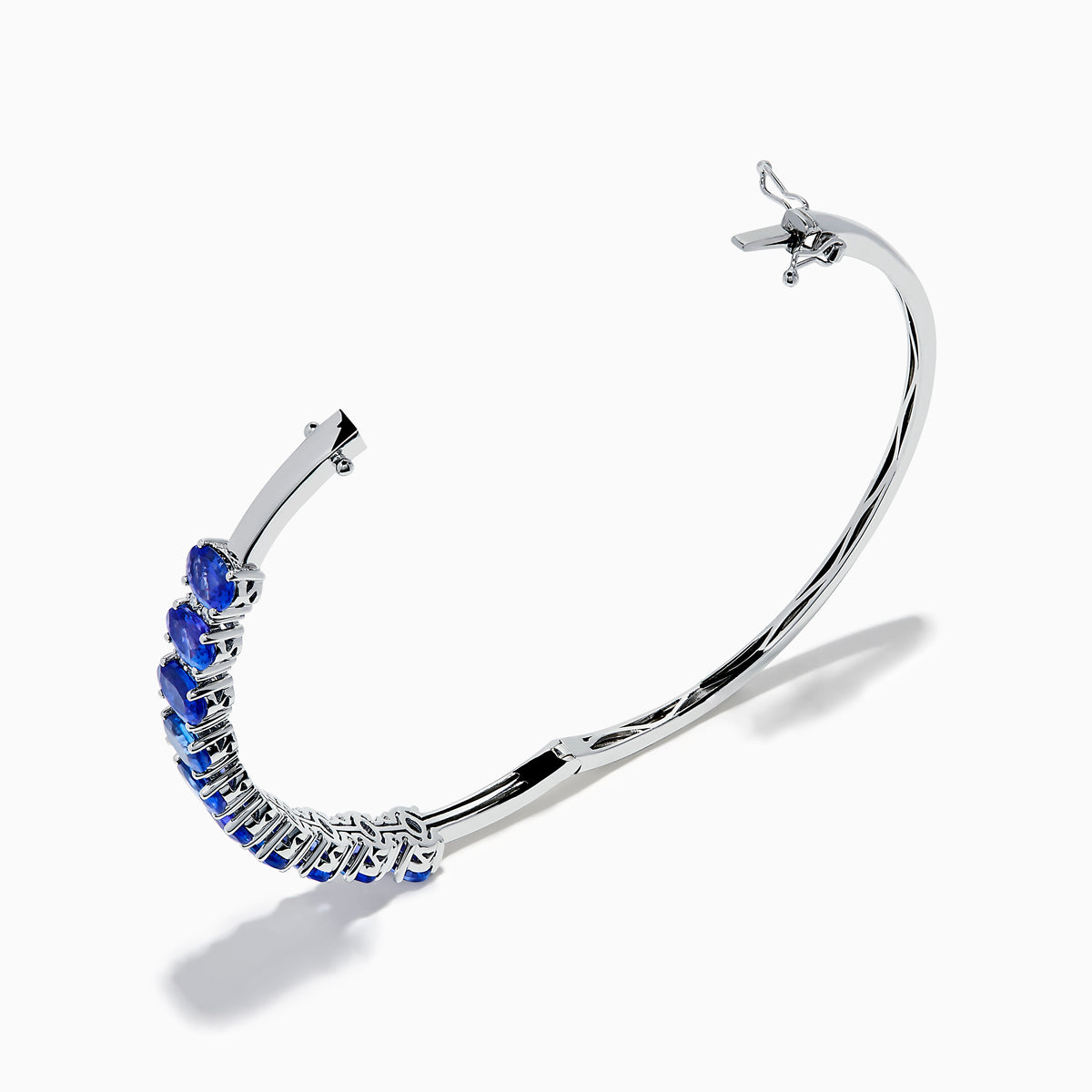 The 14K White Gold Tanzanite and Diamond Bangle features a row of oval-shaped blue tanzanites set in the center, displayed against a white background.