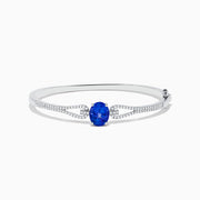 The 14K White Gold Tanzanite and Diamond Bangle showcases a striking round tanzanite centerpiece, accented by rows of sparkling diamonds along the band.
