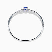 The 14K White Gold Tanzanite and Diamond Bangle showcases a striking round tanzanite centerpiece, accented by rows of sparkling diamonds along the band.