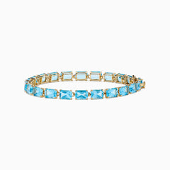The Ocean Bleu 14K Yellow Gold Radiant Cut Blue Topaz Tennis Bracelet features rectangular blue topaz gemstones set in individual links, displayed on a plain white background.