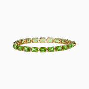 The 14K Yellow Gold Radiant Cut Peridot Tennis Bracelet features rectangular green peridot gemstones evenly spaced and connected, displayed on a white background.