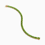 The 14K Yellow Gold Radiant Cut Peridot Tennis Bracelet features rectangular green peridot gemstones evenly spaced and connected, displayed on a white background.