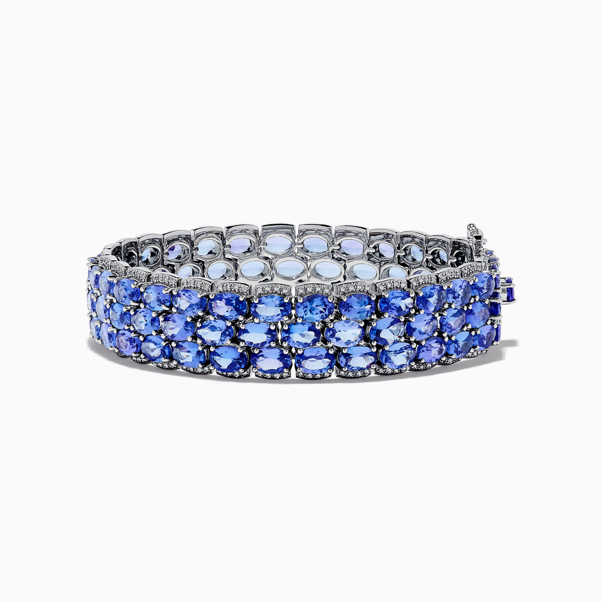 The Nahla Siri Sterling Silver Tanzanite and Diamond Bracelet features three rows of oval-cut tanzanite gemstones in prong settings on an intricate, reflective sterling silver band, displayed against a white background.