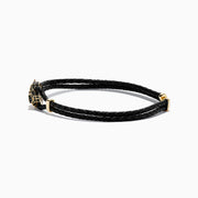 A black braided leather bracelet featuring a signature 14K yellow gold panther center with black diamond and tsavorite accents, finished with a gold clasp for men.