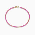 The 14K Yellow Gold Pink Sapphire Tennis Bracelet features small round pink sapphires in a continuous yellow gold setting with a gold clasp, displayed on a white background.