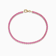 The 14K Yellow Gold Pink Sapphire Tennis Bracelet features small round pink sapphires in a continuous yellow gold setting with a gold clasp, displayed on a white background.