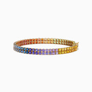 The Watercolors 14K Yellow Gold Multi Sapphire Double Lined Tennis Bracelet showcases two rows of sapphires in a vibrant rainbow gradient, with colors flowing from red and orange to yellow, green, blue, and purple.
