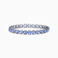 The Nahla Siri Sterling Silver Tanzanite Tennis Bracelet showcases a row of round, faceted tanzanite gemstones in prong settings, elegantly displayed against a white background.