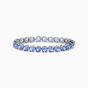The Nahla Siri Sterling Silver Tanzanite Tennis Bracelet showcases a row of round, faceted tanzanite gemstones in prong settings, elegantly displayed against a white background.