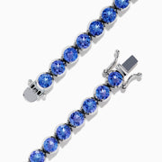 The Nahla Siri Sterling Silver Tanzanite Tennis Bracelet showcases a row of round, faceted tanzanite gemstones in prong settings, elegantly displayed against a white background.