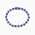 The Nahla Siri Sterling Silver Tanzanite and Diamond Tennis Bracelet features triangular blue gemstones and diamonds set in sterling silver, evenly spaced and connected, shown against a white background.