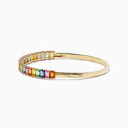 The Watercolor 14k Yellow Gold Emerald Cut Multi Sapphire Bangle features multicolored gemstones in a continuous row, creating a vibrant look.