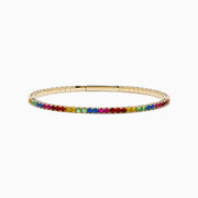 The Watercolors 14K Yellow Gold Multi Sapphire Bangle features a slim yellow gold band adorned with a row of rainbow-hued sapphires along the outer edge, shown on a white background.