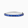 The Nahla Siri 925 Silver Tanzanite Bangle features a polished band set with sparkling blue gemstones, displayed on a white background.