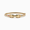 The Signature 14K Yellow Gold Multi Sapphire and Diamond Panther Bangle features two interlocking panther head motifs at the center, adorned with colorful sapphires and small diamonds.