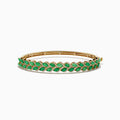 The 14K Yellow Gold Emerald and Diamond Marquise Leaf Bangle showcases an intricate leaf design with alternating emeralds and diamonds set along the band.