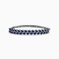 The 14K White Gold Sapphire and Diamond Leaf Motif Bangle features an elegant repeating leaf design with alternating blue sapphires and clear diamonds.