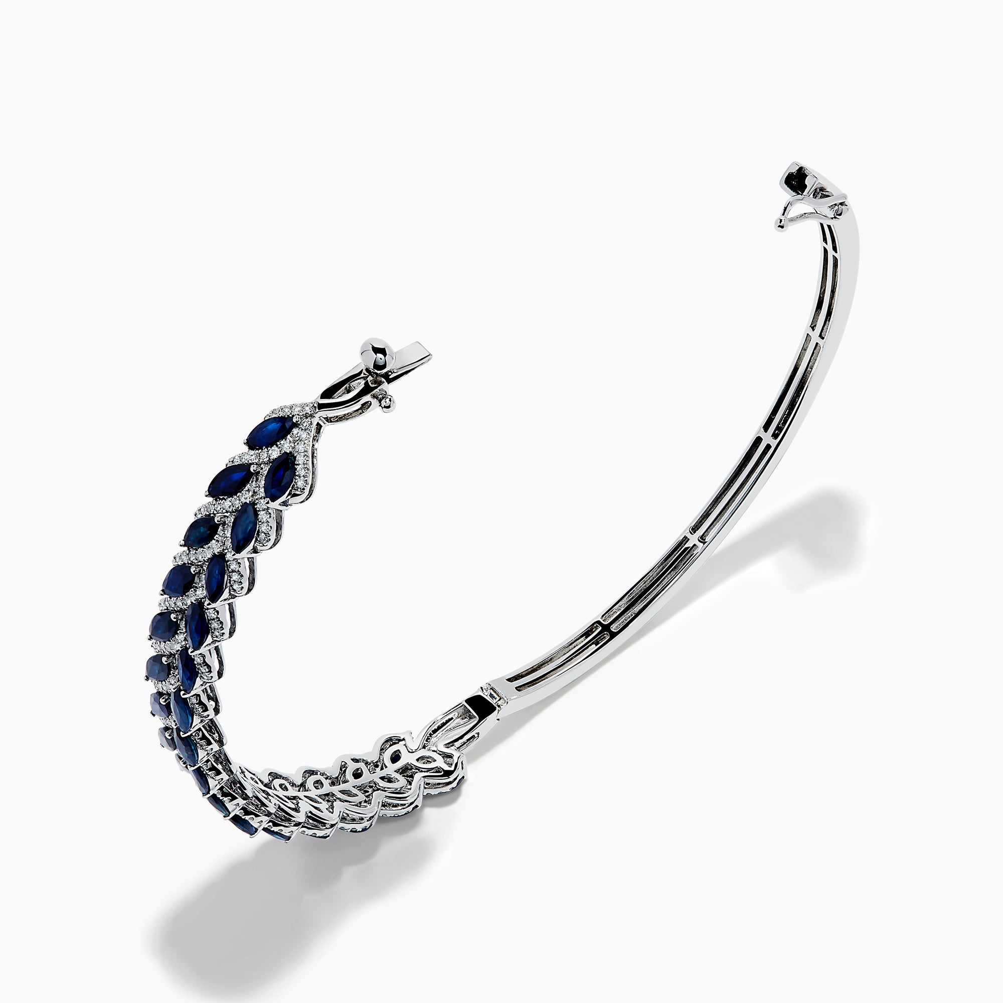 The 14K White Gold Sapphire and Diamond Leaf Motif Bangle features an elegant repeating leaf design with alternating blue sapphires and clear diamonds.