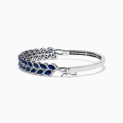 The 14K White Gold Sapphire and Diamond Leaf Motif Bangle features an elegant repeating leaf design with alternating blue sapphires and clear diamonds.