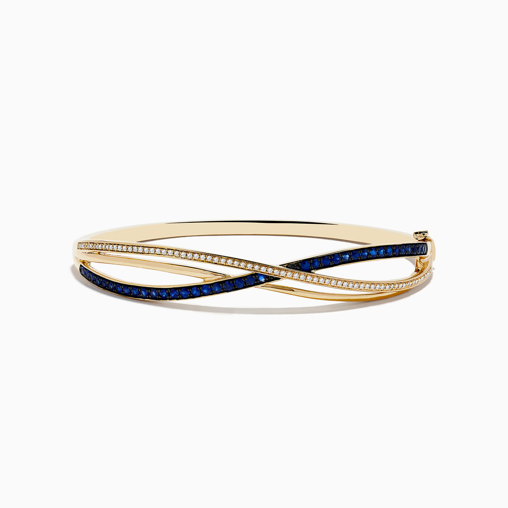 The Royal Bleu 14K Yellow Gold Blue Sapphire and Diamond Bangle showcases two intertwined bands—one set with diamonds, the other with vivid blue sapphires—in a graceful crisscross design.