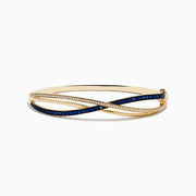 The Royal Bleu 14K Yellow Gold Blue Sapphire and Diamond Bangle showcases two intertwined bands—one set with diamonds, the other with vivid blue sapphires—in a graceful crisscross design.
