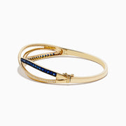 The Royal Bleu 14K Yellow Gold Blue Sapphire and Diamond Bangle showcases two intertwined bands—one set with diamonds, the other with vivid blue sapphires—in a graceful crisscross design.