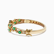 The 14K Yellow Gold Emerald and Diamond Bangle features oval green gemstones, sparkling white diamonds, an elegant openwork design, and a secure clasp.
