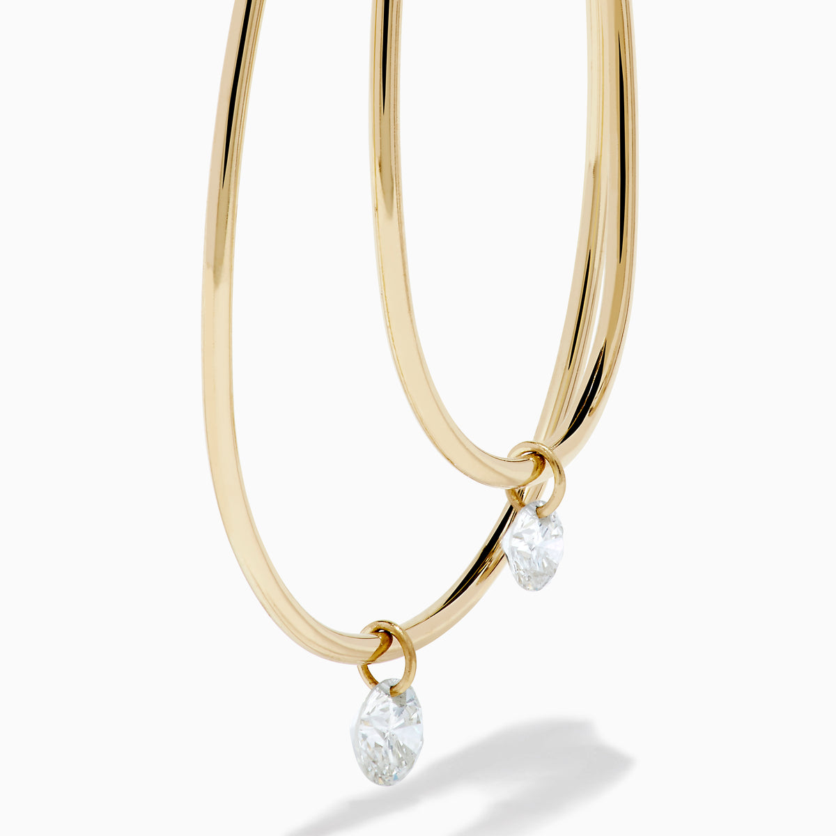 The 14K Yellow Gold Floating Diamond Double Hoop Earrings feature two elongated hoops in yellow gold, each accented with a small floating diamond, and are displayed against a plain white background.