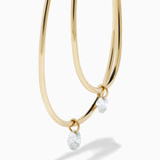 The 14K Yellow Gold Floating Diamond Double Hoop Earrings feature two elongated hoops in yellow gold, each accented with a small floating diamond, and are displayed against a plain white background.