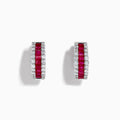 The 14K White Gold Ruby and Diamond Huggie Earrings feature a central row of square-cut red rubies, flanked by rows of round diamonds for extra brilliance.